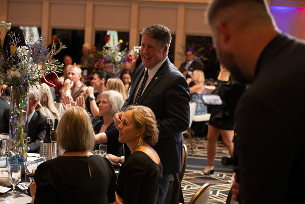 An Auto Show Gala unfolded as a formal event with people elegantly dressed in business attire, mingling both sitting and standing amidst the grandeur of a decorated banquet hall.