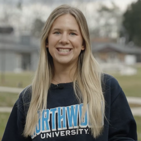 A young woman with long blonde hair wearing a Northwood University sweatshirt and smiling at the camera