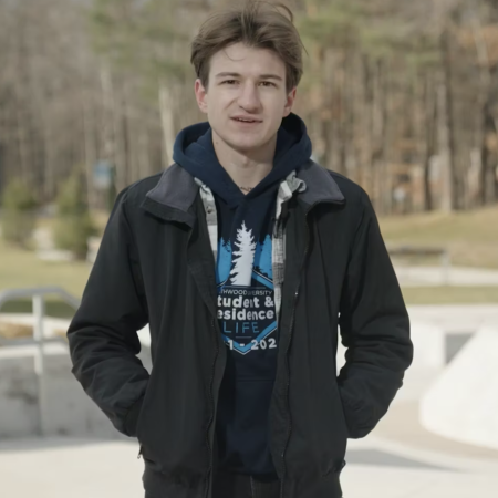 A photo of a man with short brown hair, a blue hoodie, and a jacket standing outside on the Mall Walk.