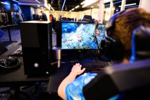 In a room reminiscent of a tech hub, a person wearing headphones is deeply engrossed in a video game displayed on a large monitor.