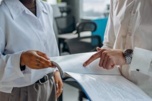 In an office setting, two people in white shirts are deeply engaged in a discussion, as one points at a page while the other holds the paperwork.